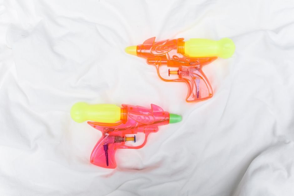 Two vibrant plastic water guns on a soft white fabric, ready for summer fun.